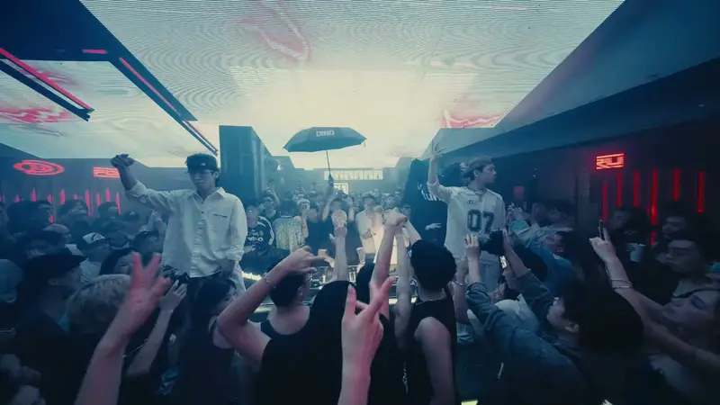 Nghệ sĩ đứng trên bốt DJ KHU 13 giữa đám đông giơ tay dưới trần sáng